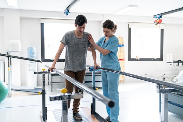 Image shows man learning how to walk again with the help of a nurse.